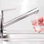 Man pouring glass of clean tap water in sink